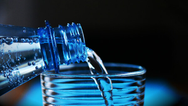 Sie sehen eine Wasserflasche, aus der Wasser in ein Glas gefüllt wird.