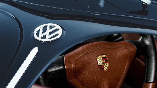 Sie sehen eine Fotomontage aus der Motorhaube eines VW Käfer und dem Lenkrad eines Porsche Carrera.