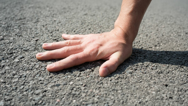 Sie sehen eine Hand, die falsch auf Asphalt gedrückt wird.
