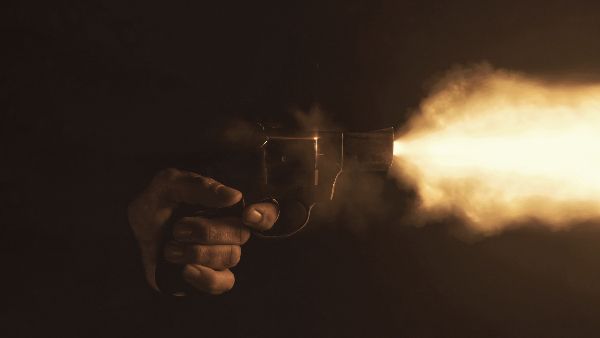 Sie sehen die Nahaufnahme eines Revolvers, der mit einem hellen Blitz in einer dunklen Umgebung abgefeuert wird.