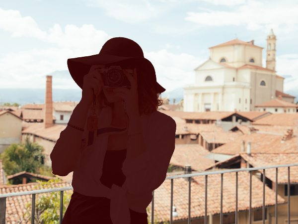 Sie sehen eine mediterrane Stadt und davor eine Frau, die Urlaubsfotos macht. Die Frau ist allerdings nur als Silhouette dargestellt, ganz so als wäre sie ausradiert worden.