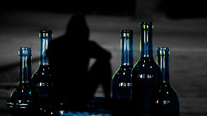 Sie sehen leere Flaschen mit einen schwarzen Schatten einer Person im Hintergrund.
