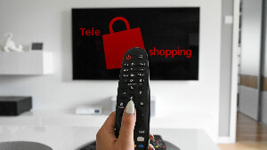 Sie sehen einen Fernseher in einem Wohnzimmer, auf dem ein Logo mit dem Schriftzug &bdquo;Teleshopping&ldquo; zu sehen ist.