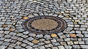Sie sehen ein Kopfsteinpflaster mit einem eingelassenen Gullideckel.