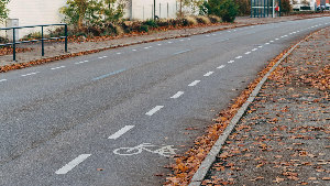 Sie sehen eine Straße in einem Ort, auf der ein Teil der Fahrbahn als Streifen für Radfahrer markiert wurde.