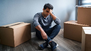 Sie sehen einen traurigen (verzweifelten) Mann, der in einem leeren Zimmer mit Umzugskartons sitzt.