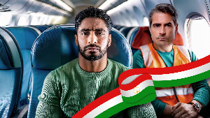 Sie sehen zwei traurige Personen im einem Flugzeug, wobei eine mit einer Warnweste bekleidet ist.