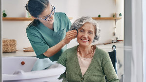 Sie sehen eine Pflegekraft, die einer älteren Dame beim Waschen hilft.