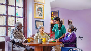 Sie sehen eine Pflegekraft, die mehreren älteren Personen Gesellschaft leistet.