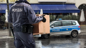 Sie sehen einen Polizisten, der eine Umzugskiste zu seinem Streifenwagen trägt.