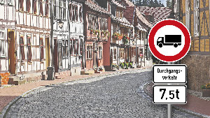 Sie sehen ein Verkehrsschild, welches die Durchfahrt für LKW über 7,5t Gesamtgewicht verbietet, vor der Kulisse einer Kleinstadt.