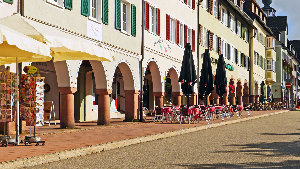 Sie sehen einen Fußweg in einer Stadt, auf dem Tische und Stühle eines Restaurants stehen.