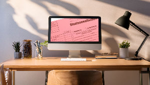 Sie sehen einen Schreibtisch mit einem Computer, auf dem das Bild einer Strafakte zu sehen ist.