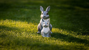 Sie sehen zwei Hasenfiguren, die voreinander im Gras sitzen.