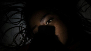 Sie sehen ein trauriges Mädchen in der Duneklheit, davor ein Handy.