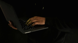 Sie sehen zwei Hände in der Dunkelheit, die einen Notebook halten und etwas tippen.