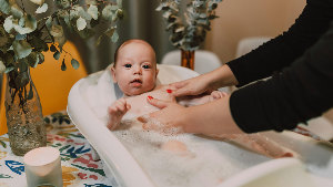 Sie sehen ein Kleinkind das in einer Badewanne gebadet wird.