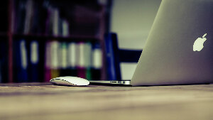 Sie sehen ein Macbook auf einem Schreibtisch stehen.