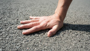 Sie sehen eine Hand, die falsch auf Asphalt gedrückt wird.