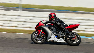 Sie sehen einen Motorradfahrer in voller Ausrüstung, der schnell über die Rennstrecke Hockenheim in Deutschland auf einem Yamaha-Motorrad navigiert.