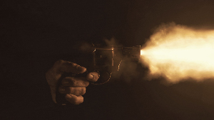 Sie sehen die Nahaufnahme eines Revolvers, der mit einem hellen Blitz in einer dunklen Umgebung abgefeuert wird.